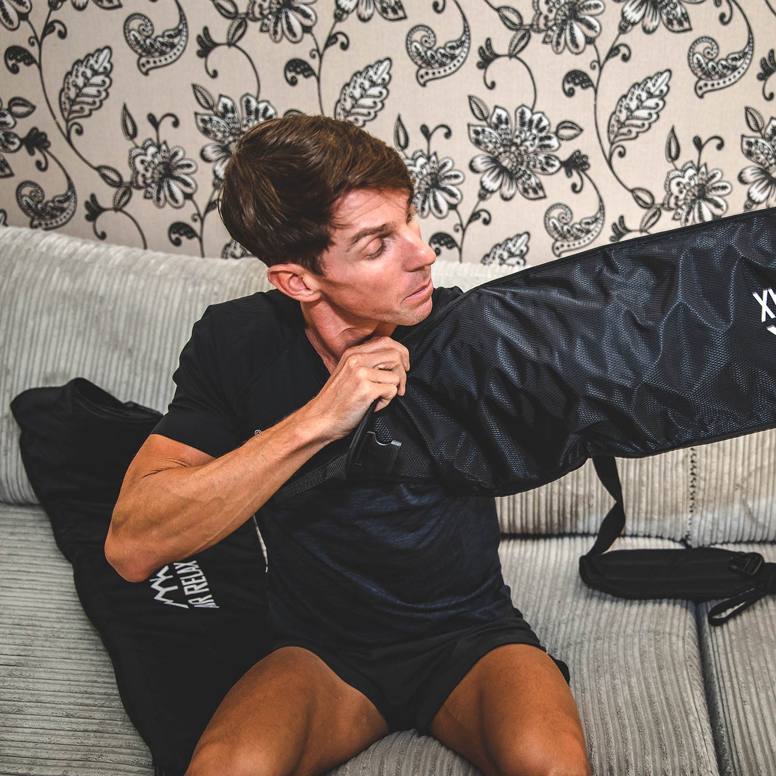 AIR RELAX PRO AR-4.0 ARM SLEEVE — Man zipping up his arm sleeve on couch