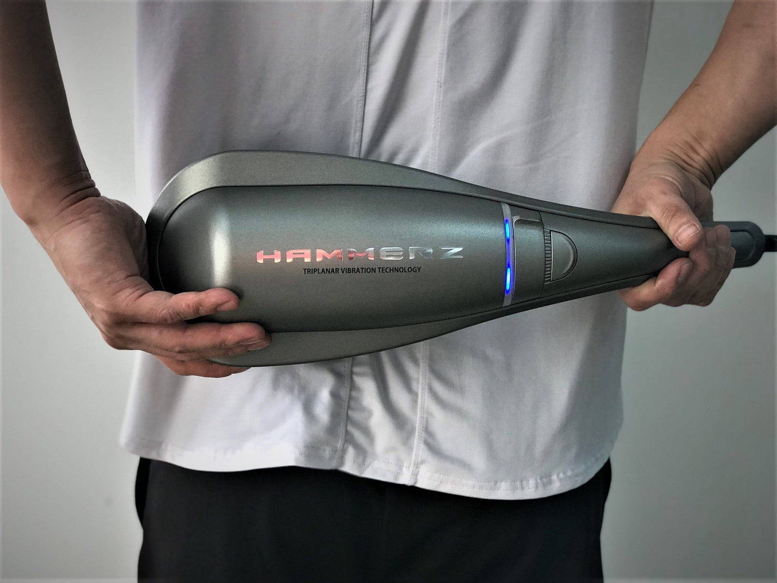 HAMMERZ MASSAGE DEVICE WITH TRIPLANAR VIBRATION TECHNOLOGY — Close-up of a person holding the massager horizontally showing the illuminated Hammerz logo